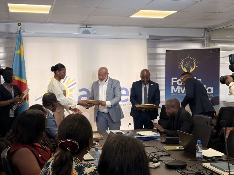 Remise d'un certificat à une participante, devant le logo de l'ANSER et le drapeau de la République démocratique du Congo.